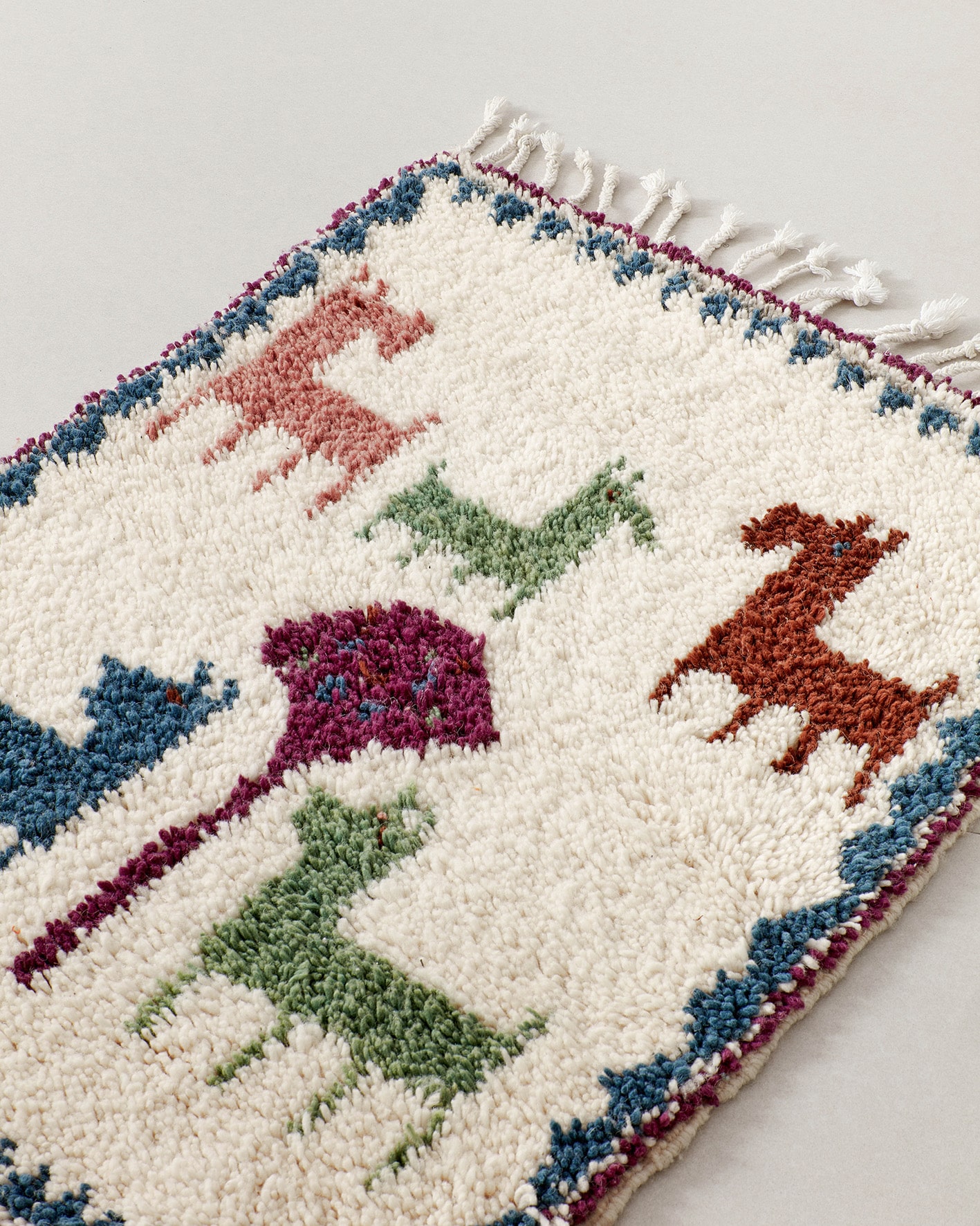 Tiny rug featuring animals in blue-green-burgundy colours, close