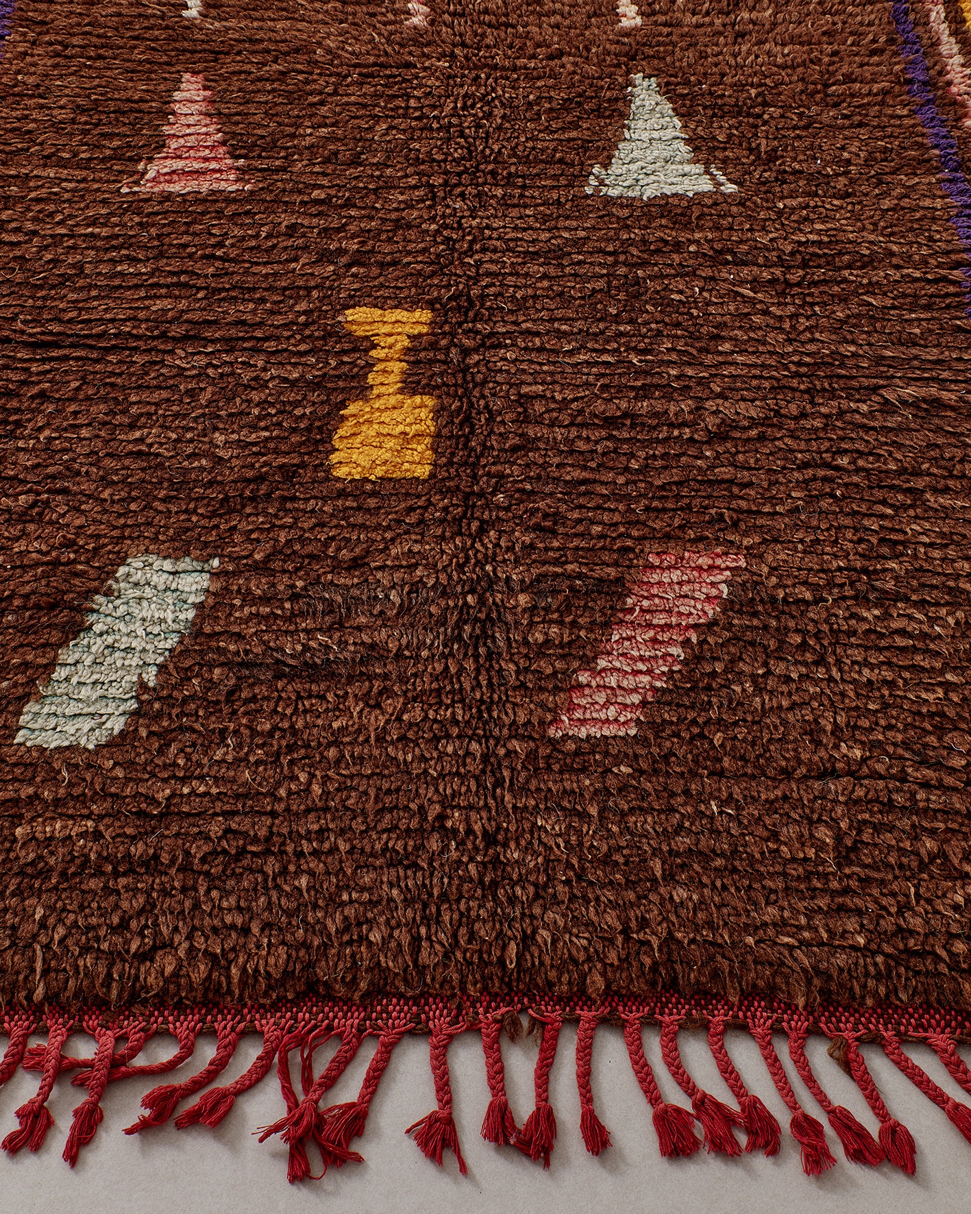 Brown rug with small pastel pictograms, fringes